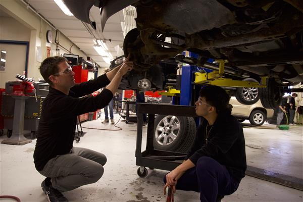 Students work on the underside of an elevated car in their automotive class of Hoffman Estates High School.