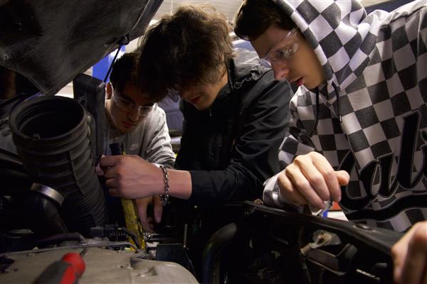 Students work together in automotive class as they lean in to examine under the hood.